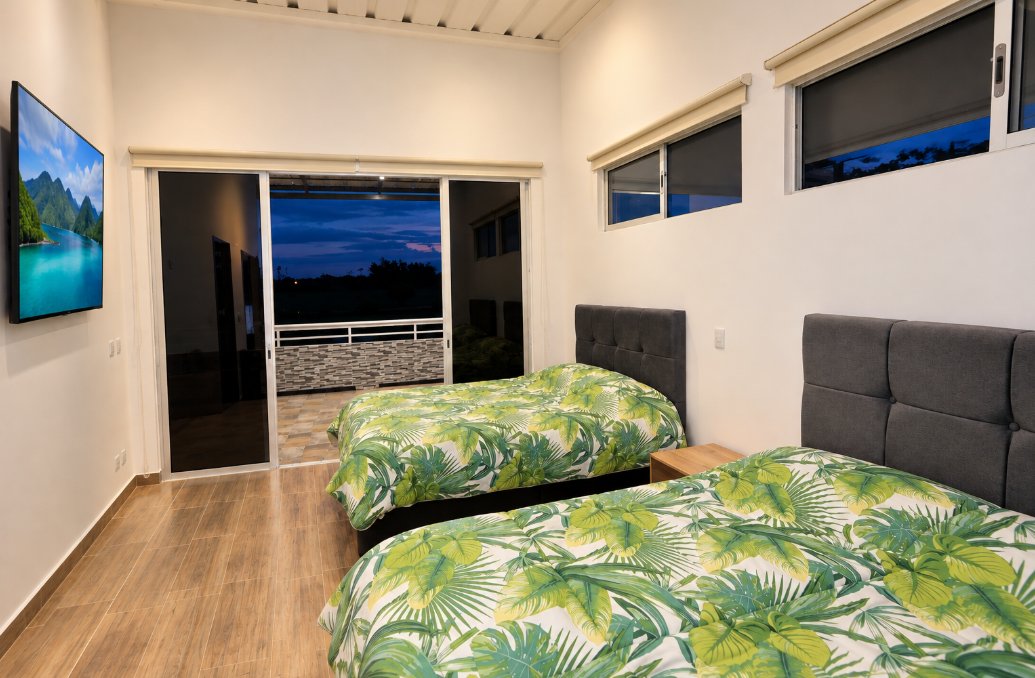 Habitación de huéspedes de Finca Mana con dos camas, televisor y salida a la terraza al atardecer
